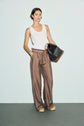 Woman stands against a pale background wearing a white sleeveless top, édition limitée patterned wide-leg pants, and sandals, holding a large black and brown monogramme tote bag.
