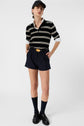 Person wearing a black cap, striped black and white shirt, navy shorts with a belt, black socks, and black shoes stands against a plain white background.