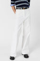 Person wearing loose-fitting white pants in a coupe large style, a black belt, black shoes, and a navy blue and white striped shirt with blue and white striped sleeve cuffs. The photo is cropped at the shoulders.