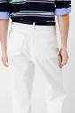 A person wearing a navy and white striped shirt with rolled-up sleeves and a coupe large jean blanc, seen from behind, standing against a plain background.