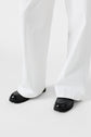 Person wearing loose white pants (coupe large) and black loafers standing on a white background.