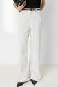 Person wearing high-waisted, white jean rayé with black vertical pinstripes, a black belt, and black pointed shoes. They are also holding a black clutch under one arm. Only the lower half of the body is visible.