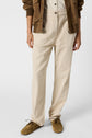 Person wearing a beige pantalon lin, brown shoes, a white shirt, and a brown jacket. Only the lower half of the body is visible against a plain light background.