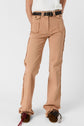A person wearing tan frayed seam coupe flare pants with large front pockets, a black woven belt, and brown moccasins with decorative tassels, standing against a plain white background.