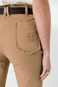 Close-up of a person wearing tan coupe flare pants with a frayed back pocket, a woven dark brown belt, and a gold ring. The person’s hand is relaxed at their side. The background is plain and light-colored.