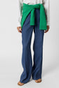 Person wearing blue wide-leg pants, a white shirt, and tan sandals, with a bright green sweater tied around their waist, standing against a plain white background.
