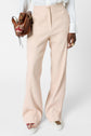 A person wearing wide-leg beige pants, white shirt, and white sneakers with love décor, holding a brown leather handbag with tassels.