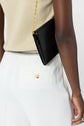 A person wearing élégant pantalon femme blanc en microfibre and a beige top carries a black purse with a gold chain strap over their shoulder. The image is cropped to show only the torso and upper legs.