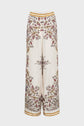 Cream-colored wide-leg pants with a paisley and floral print in burgundy, brown, and gold tones. Pants have a gold trim at the waistband and cuffs.