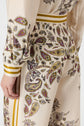 A close-up of a cream-colored outfit with yellow, purple, and black paisley patterns. The persons left arm is relaxed at their side, and the clothing has yellow stripes on the waistband and cuffs.
