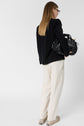 A woman with straight blonde hair, wearing glasses, a black blazer, and metallic shoes, holds a large black handbag while facing away from the camera against a plain background. She completes her look with white coton pantalon de jogging featuring a subtle logo GD.