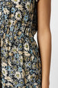 A close-up of a person wearing a sleeveless dress with a floral pattern featuring white, yellow, and blue flowers, shown from the shoulder to the waist. Only one arm is visible.