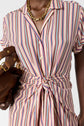 A person wearing a pink striped robe chemise button-down dress with a front tie, gold chain necklace, and holding a brown handbag with gold hardware.