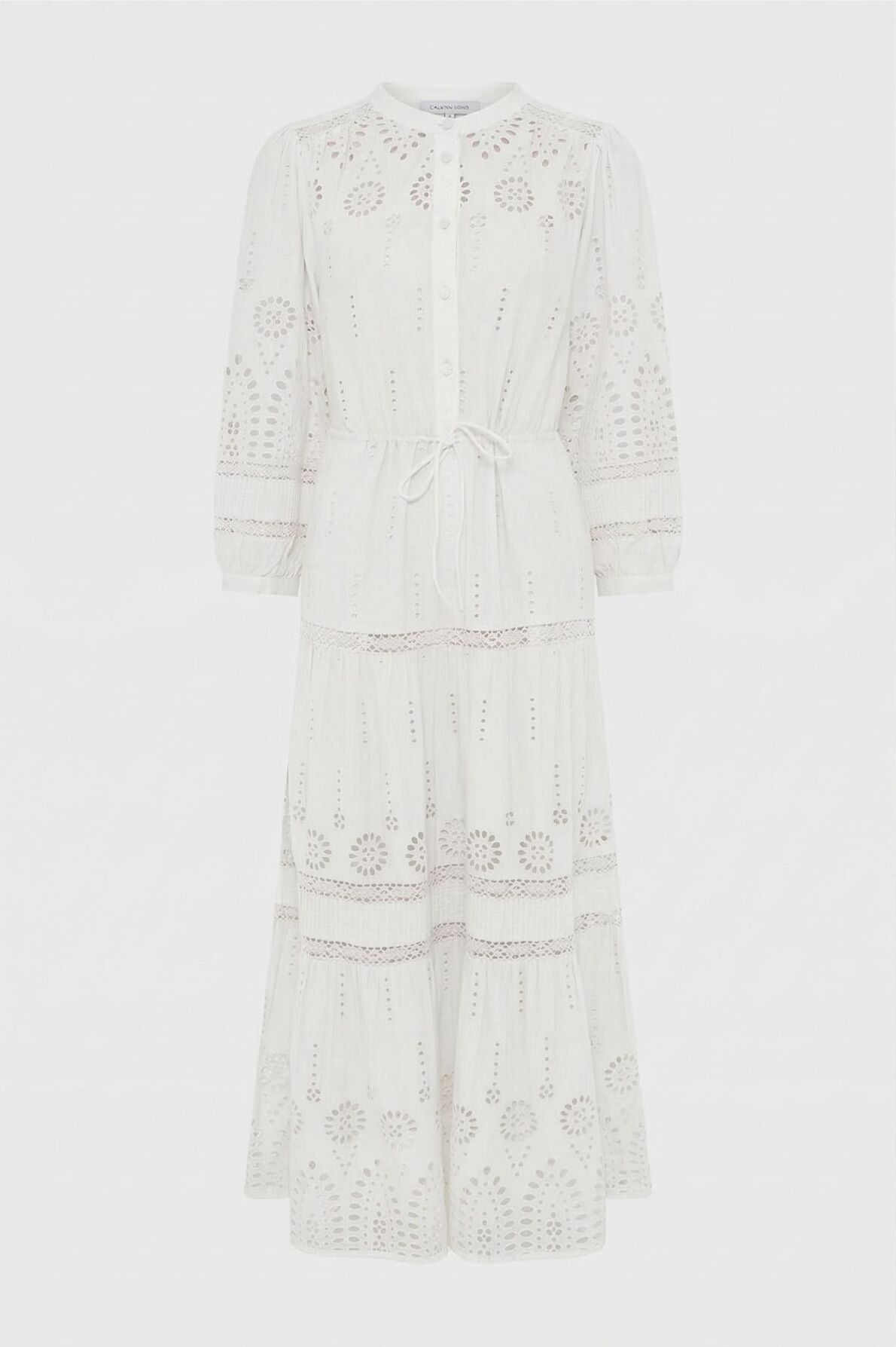 White, long-sleeve, button-up midi dress with intricate eyelet embroidery, cinched waist with a tie belt, and a tiered skirt. The dress has a delicate, airy appearance and features floral cutout patterns throughout.