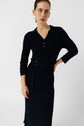 A woman in a navy blue robe longue en maille côtelée, à col polo et manches longues, avec une ceinture à la taille, se tient contre un fond blanc uni, regardant l’objectif avec une expression neutre.