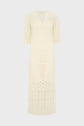 Cream-colored, knee-length crochet dress with short sleeves and a V-neckline, displayed on a plain light background. The dress features intricate, semi-sheer knit patterns throughout.