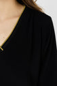 A close-up of a person wearing a black V-neck top with a decorative yellow and black trim along the neckline. Only the shoulder, neckline, and part of the upper chest are visible.
