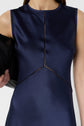 A woman wearing a sleeveless, navy blue satin dress with decorative stitching detail, holding a black clutch under her arm.
