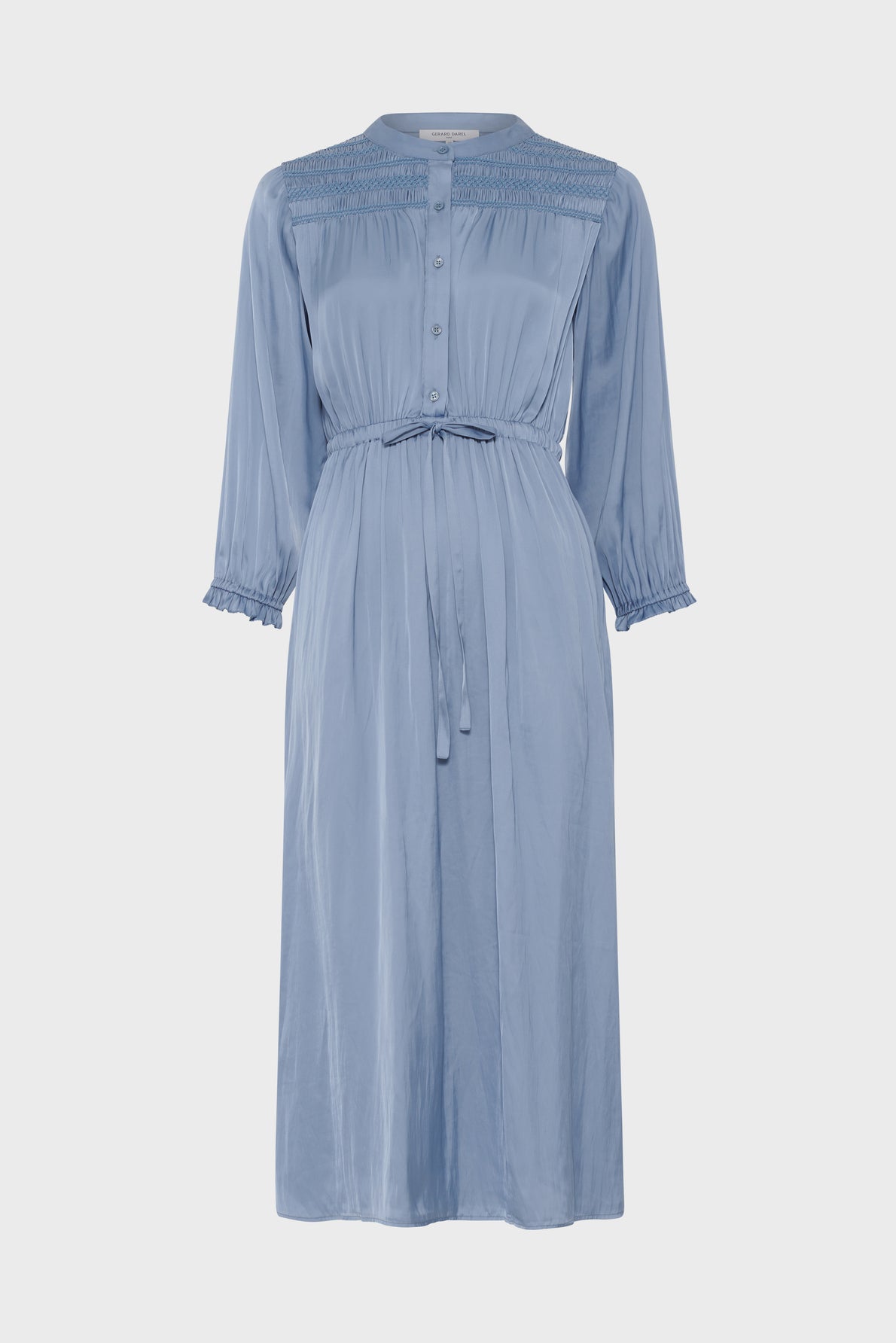 Light blue, long-sleeve midi dress with a button-up front, cinched waist with tie belt, pleated detailing on the chest, and ruffled cuffs. The dress has a soft, flowy fabric and a modest collar.
