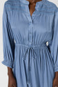 A person wearing a light blue, long-sleeved, button-up dress with a drawstring waist and gathered details at the shoulders and cuffs.