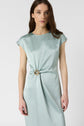 Woman wearing a light blue, cap-sleeve dress with a knot and gold ring detail at the waist, standing against a plain white background.