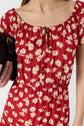 Woman wearing a red dress with a white daisy print, holding a black purse. The dress has short sleeves, gathered neckline with a tie, and an elastic waist. Only the upper body is visible.