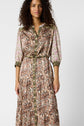 A woman with curly hair wears a long-sleeved, button-down dress featuring pink floral sleeves and a tan, brown, and green paisley pattern on the front and skirt. She is standing against a plain white background.