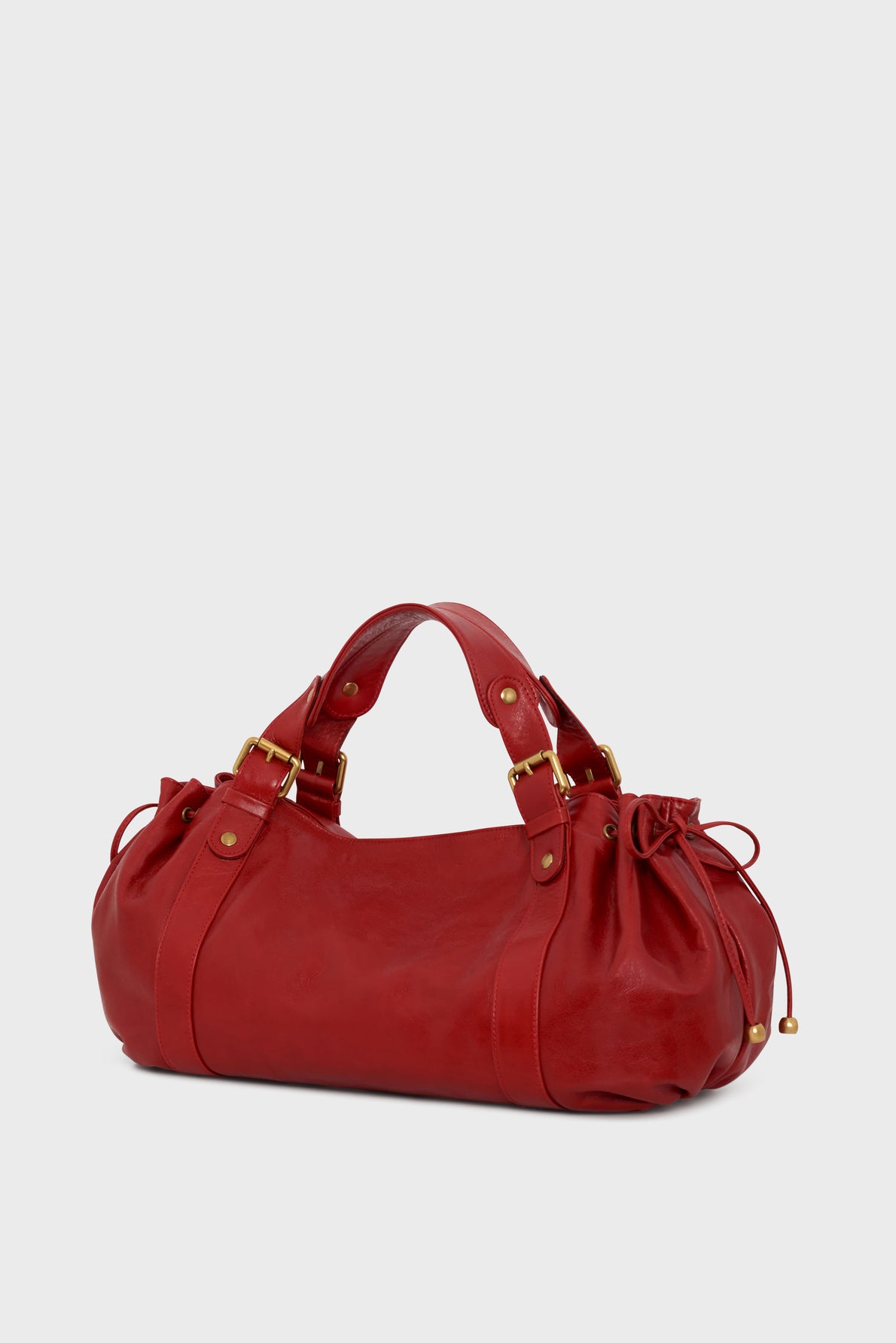 A red leather sac à main with gold hardware, two handles, and drawstring details on both ends, crafted from luxurious cuir froissé and displayed against a plain light gray background.