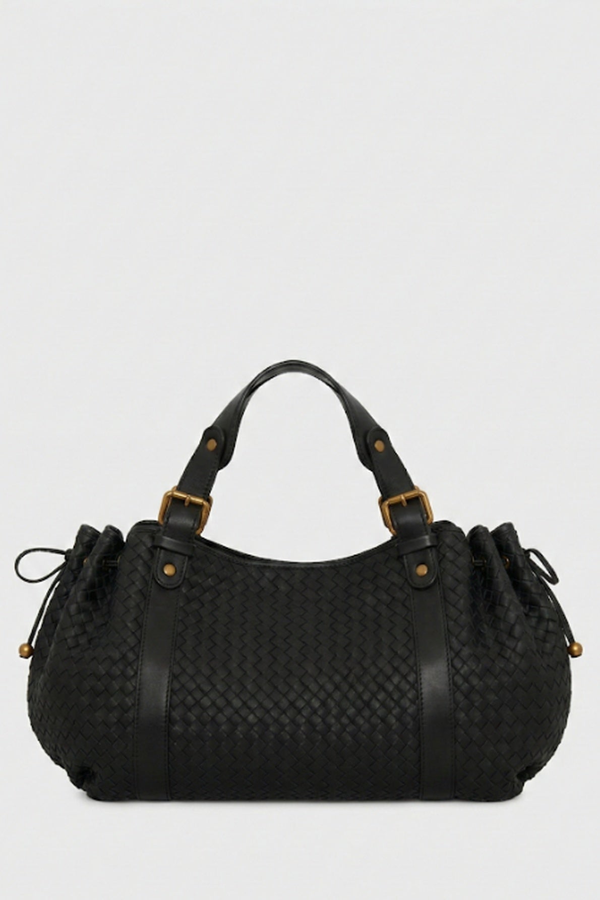 A black sac à main tressé in woven leather, crafted with savoir-faire artisanal, featuring short handles, gold hardware, and drawstring sides, displayed on a plain light gray background.