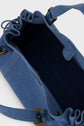Open blue fabric sac à main with a spacious, dark-lined interior, visible drawstring top, side pocket, and adjustable strap with metal hardware in toile coton—perfect as your versatile sac 24H—placed on a light background.