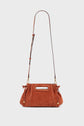 A rust-colored cuir velours sac à main with a cut-out handle and an adjustable brown leather shoulder strap, featuring gold accents and elegant drawstring details on both sides, displayed against a light gray background.