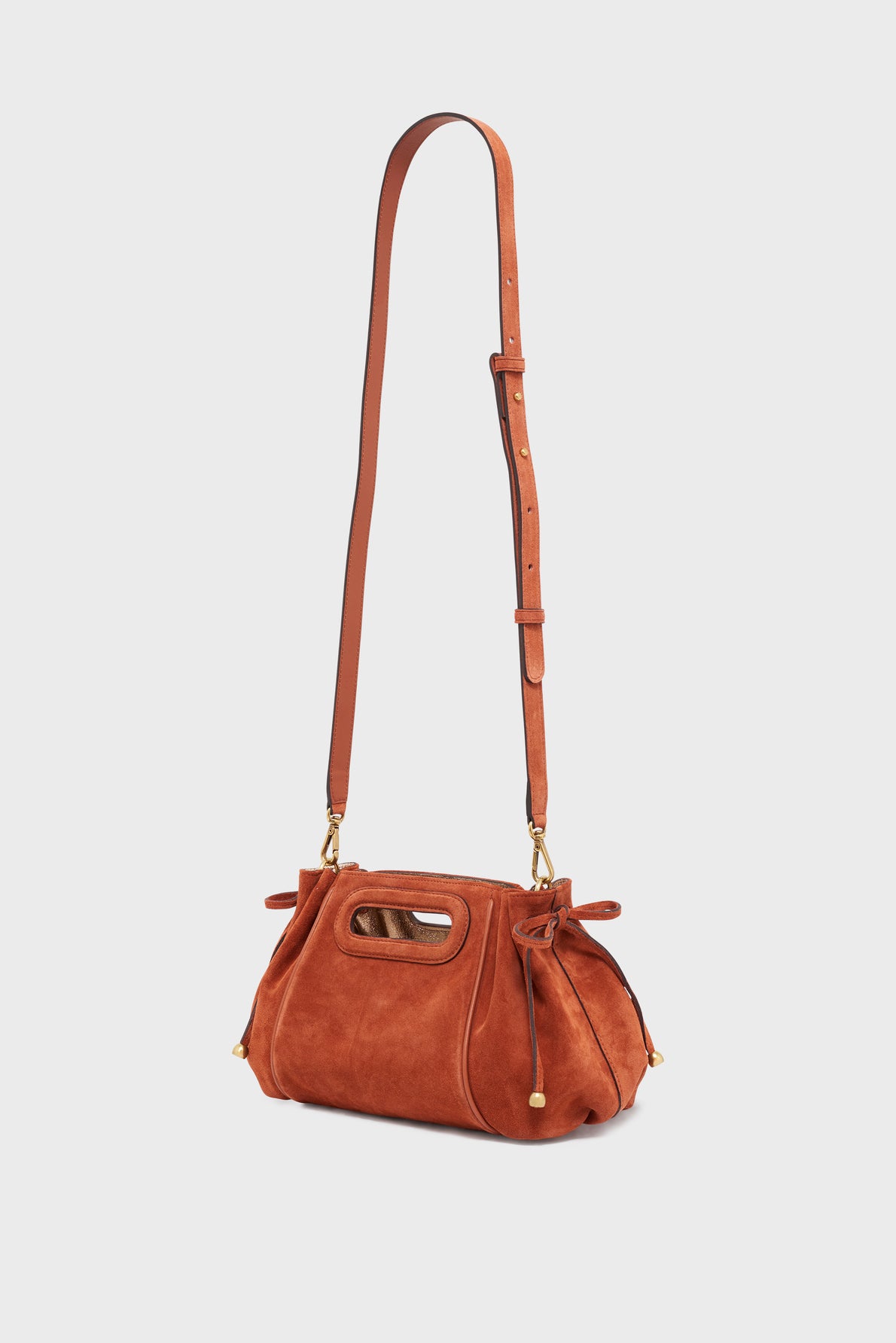 A small, rust-colored sac à main in élégant cuir velours, featuring a long adjustable strap, gold hardware, and cutout handles, displayed against a plain light background.