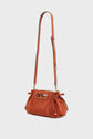 A small, rust-colored sac à main in élégant cuir velours, featuring a long adjustable strap, gold hardware, and cutout handles, displayed against a plain light background.