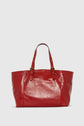 A large, shiny red leather tote bag with two adjustable shoulder straps and gold-tone buckle accents, displayed against a plain light gray background.
