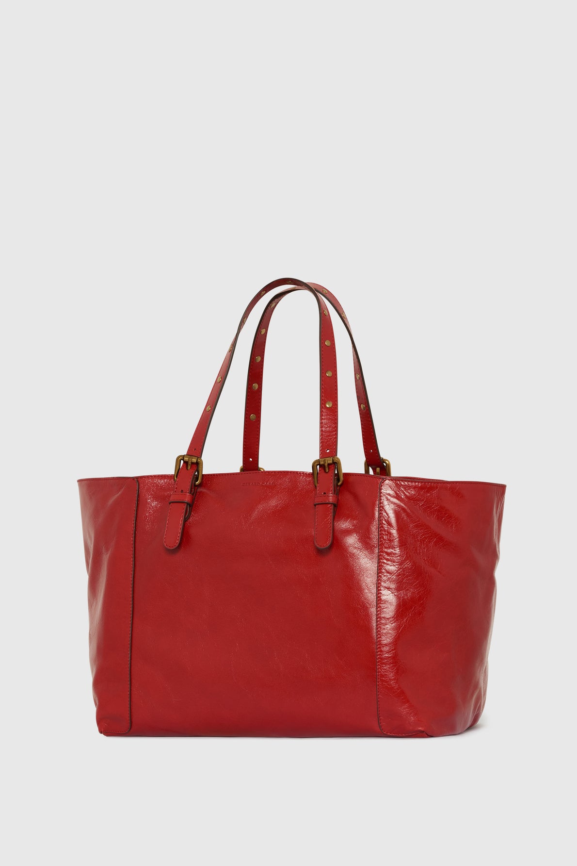 A shiny red leather tote bag with two long handles featuring gold buckles and stud details, set against a plain white background.