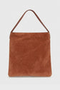 A brown cuir velours totebag with a single, flat shoulder strap, photographed against a plain light-grey background. The bag has a simple, minimalist design without visible hardware or embellishments.