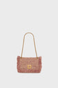 A pink woven sac bandoulière with fringe edges, showcasing savoir-faire artisanal craftsmanship, features a gold chain strap and a gold clasp closure, displayed against a plain white background.