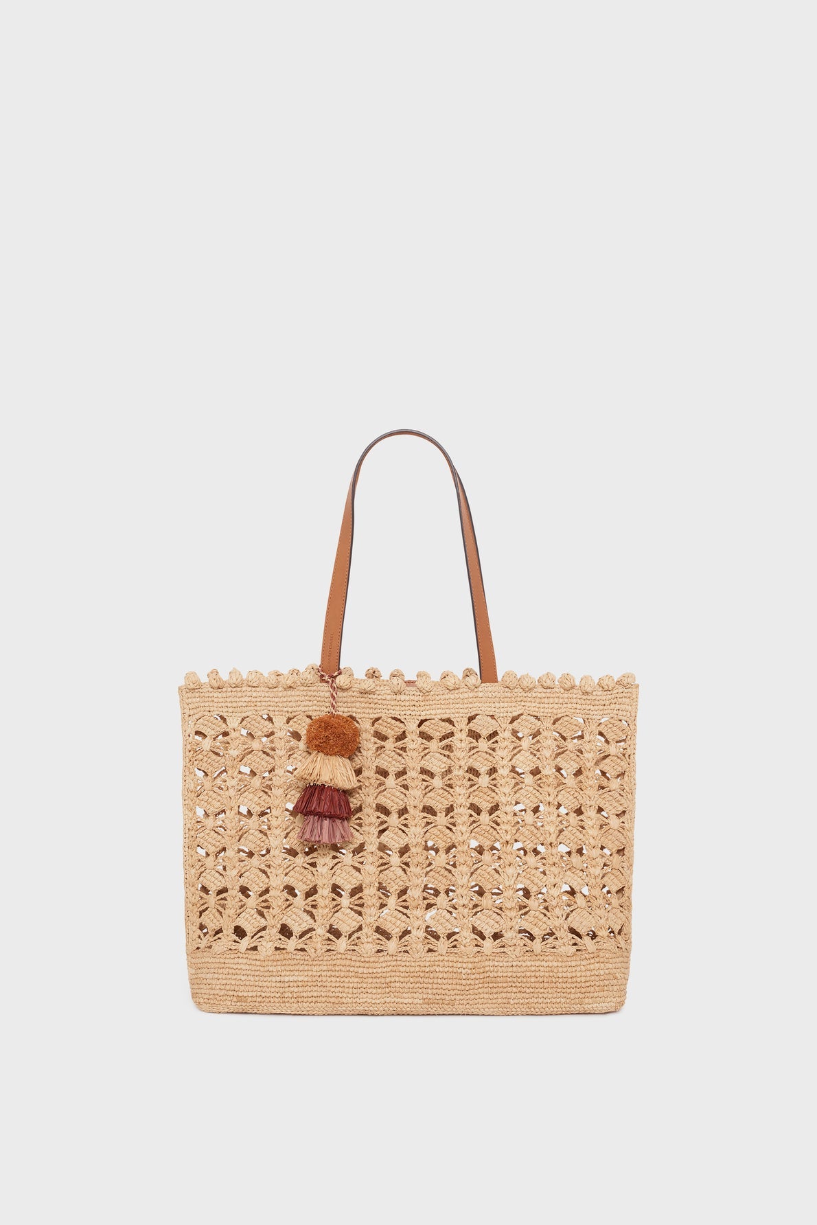Beige woven straw tote bag with two brown handles and decorative multicolored tassels hanging from one handle, this cabas raphia sac artisanal exudes a panier chic vibe, set against a plain white background.