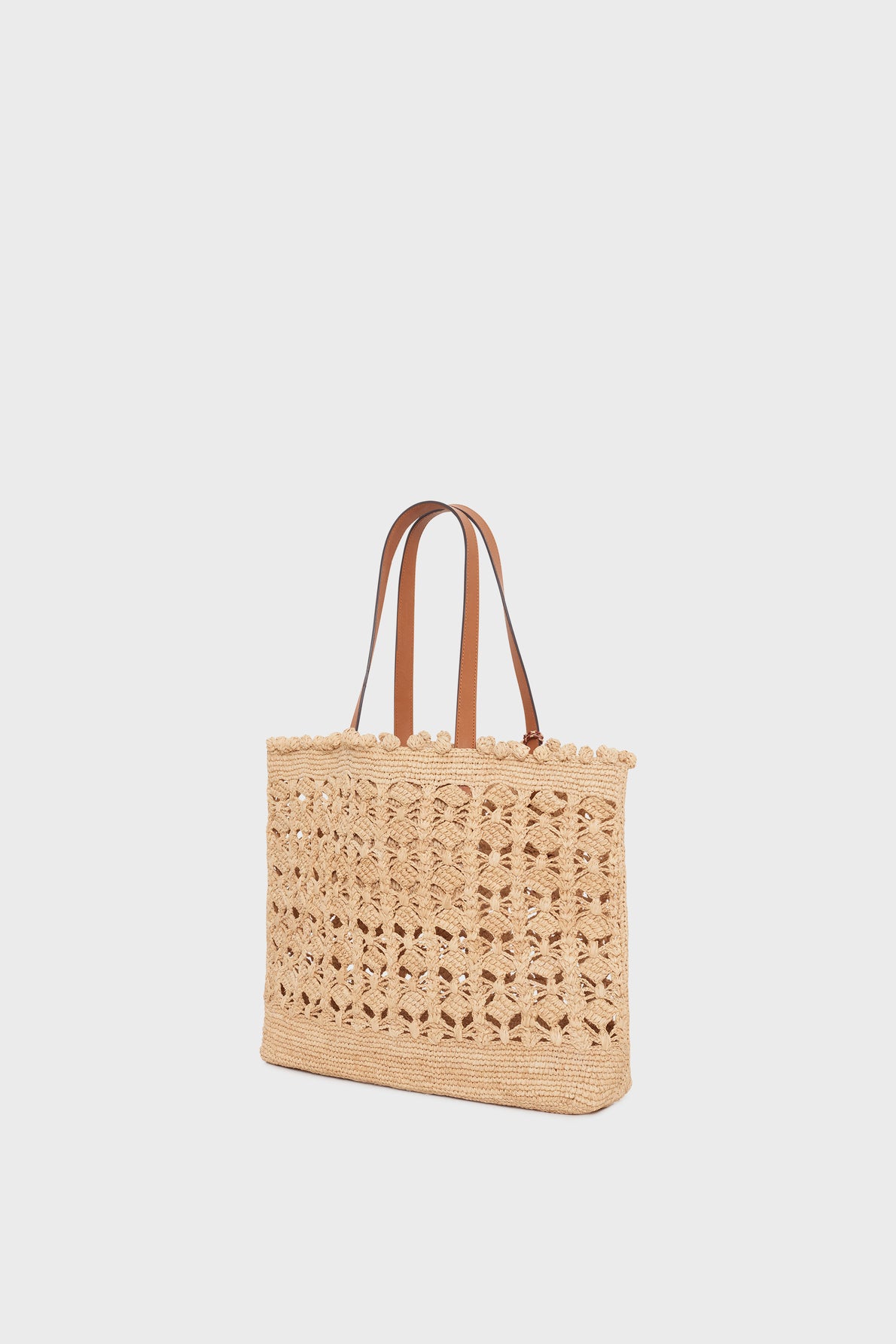 Beige woven straw tote bag with decorative openwork pattern and two brown leather shoulder straps, displayed against a plain white background—a cabas raphia élégant that perfectly embodies the essence of a panier chic.