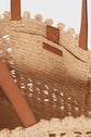 Close-up of a woven straw tote bag with brown leather handles and a small leather patch label reading Gerard Darel stitched inside. This panier chic features an open weave pattern with a decorative trim on the edge, highlighting its refined, sac artisanal craftsmanship.
