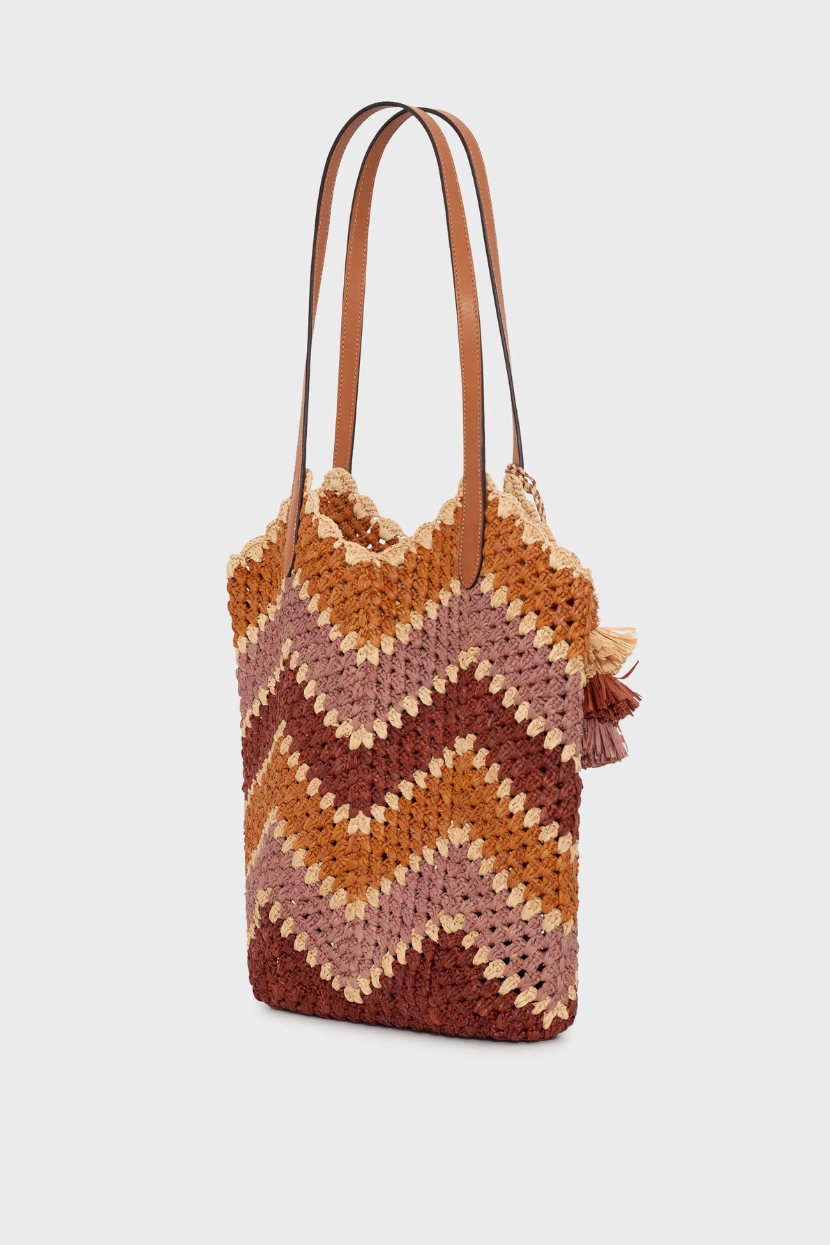 A chic sac cabas raphia with a chevron pattern in shades of brown, orange, and beige, featuring leather shoulder straps and small tassel accents on one side—perfect for elevating your style as a sac été femme.