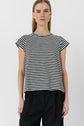 A person with straight, light brown hair wears a tee-shirt Mayane à manches courtes papillon orné de rayures noires et blanches and black pants, standing against a plain white background.