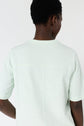 Person with short curly hair, seen from behind, wearing a light mint green short-sleeve shirt against a plain light background.