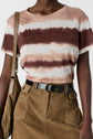A person wearing a pink, cream, and brown tie-dye t-shirt, camel-colored high-waisted skirt with belt, and carrying a tan fringed shoulder bag.