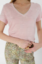 A person wearing a light pink V-neck T-shirt and floral-patterned pants, holding a brown belt with both hands. Only the torso and upper legs are visible.