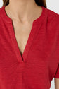 A person wearing a red V-neck shirt with a split neckline. The image is cropped to show the upper chest, neck, and part of the shoulders, but not the face.