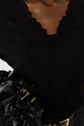 A person wearing a black V-neck top with lace detailing at the neckline holds a black leather bag with gold hardware.