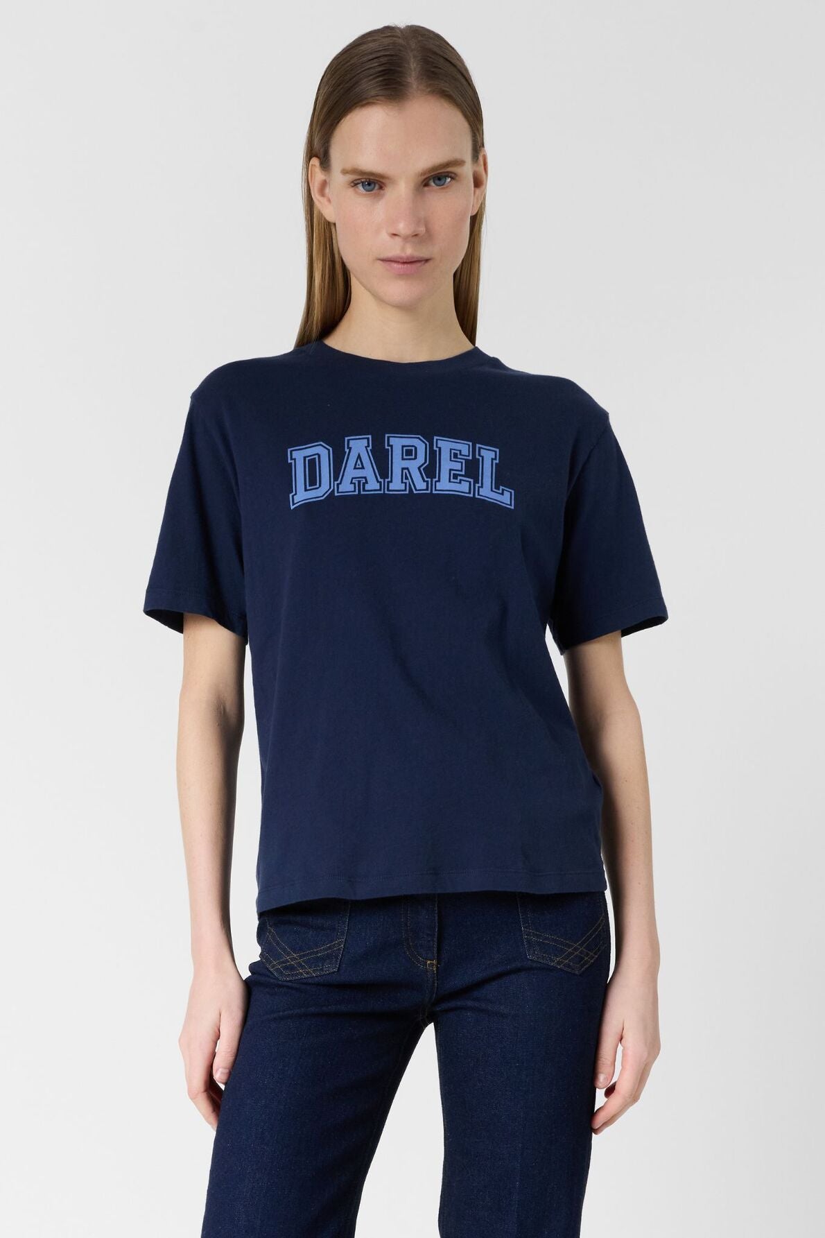 A person wearing a tee-shirt bleu marine en coton with the word DAREL in large blue letters stands against a plain light background, looking at the camera with a neutral expression.