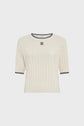 A cream-colored, short-sleeve ribbed knit sweater with black trim on the collar and cuffs, and a small black-and-white square logo on the chest.