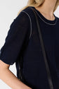 A person wearing a navy blue short-sleeve knit top with white piping along the seams and a black shoulder strap, shown from the shoulders to the waist.